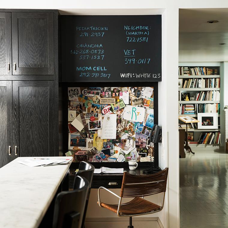 A kitchen with the top of a wall that has been painted using black using Benjamin Moore's chalkboard paint, showing family member phone numbers written in blue and white chalk. 